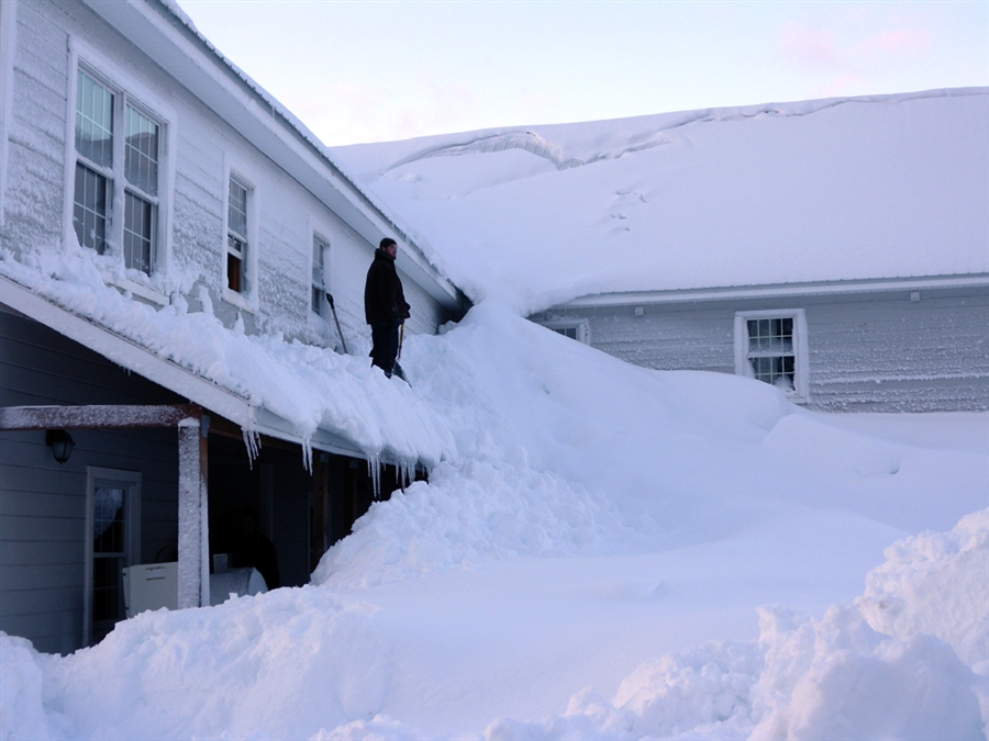 Человек стоит на крыше дома, заваленой снегом, в рыбацком городке Кордова
